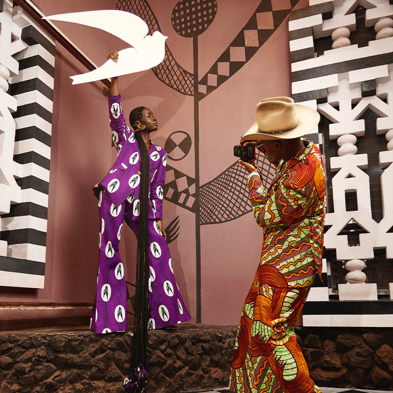 Sarah Diouf poses in bold Vlisco fabric while Trevor Stuurman photographs, set against a backdrop of striking geometric patterns — celebrating African fashion and artistry.