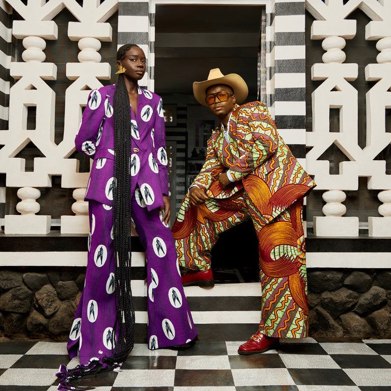 Sarah Diouf and Trevor Stuurman styled in bold Vlisco prints, posing against black-and-white patterned architecture in a contemporary African fashion photoshoot